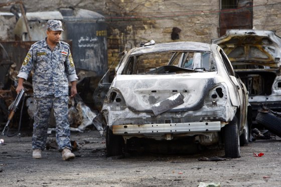Image: A police officer looks at a burnt vehicle at a parking lot after a bomb attack in Baghdad