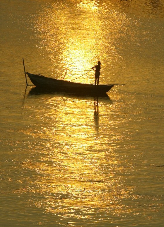 A fisherman stands in his boat at sunrise in River Ganges in Varanasi, India. With the Deserts, Palaces and Ganges package, you'll sail along the Ganges by the holy city of Varanasi, tour Delhi, ride an elephant near Jaipur, and visit the iconic Taj Mahal.