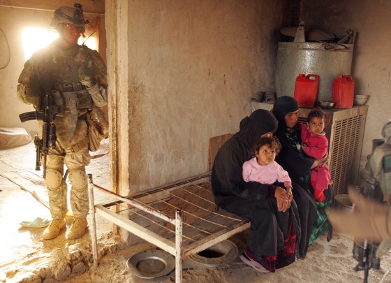 Image: An Iraqi family waits on a bench as US soldiers search their home