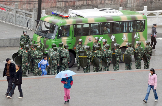 Image: Tibetans walk past Chinese paramilitary policemen patrolling in Kangding county, the capital of Ganzi Tibetan Autonomous Prefecture
