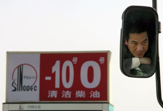 Image: A Chinese truck driver is seen in a back mirror while waiting outside a Sinopec gas station.