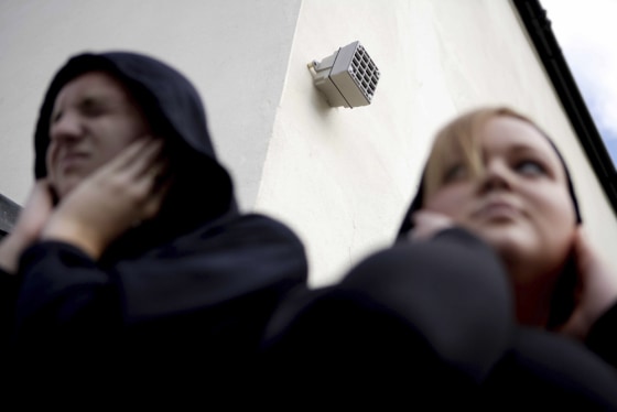 This undated photo provided by Compound Security Systems shows unidentified people holding their ears while standing under a Mosquito mounted to a wall. According to Compound Security Systems, the Mosquito is an ultrasonic device that deters teenagers with a high-pitched noise. 