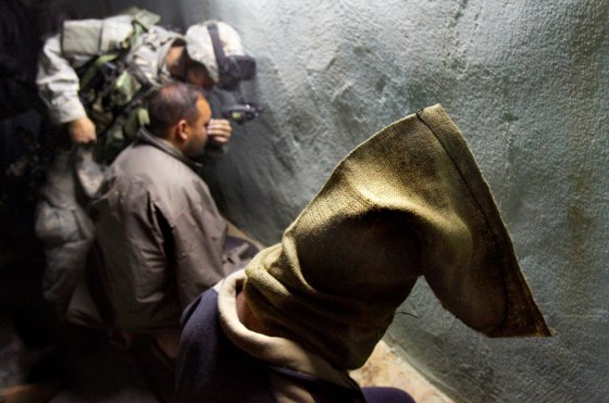 An Iraqi detainee sits with his head covered by a sand bag while an American soldier covers another detainee's eyes with tape during a raid in Ramadi on Feb. 4, 2006.