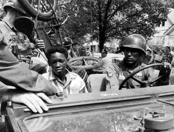 Image: Caucasian National Guardsmen give an African-American student and his bicycle a lift to school