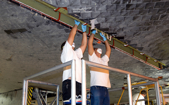 Technicians work on insulation tiles near the shuttle Discovery's landing-gear door at the Orbiter Processing Facility at NASA's Kennedy Space Center.