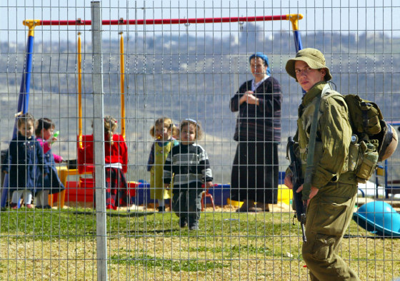 An Israeli soldier patrols the area as children play in a playground in the West Bank&nbsp;settlement outpost of Harasha, northwest of the Palestinian city of Ramallah, on Wednesday. 