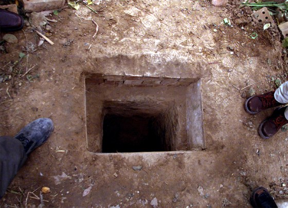 JOURNALISTS STAND BESIDE HOLE IN WHICH SADDAM HUSSEIN WAS HIDING IN TIKRIT