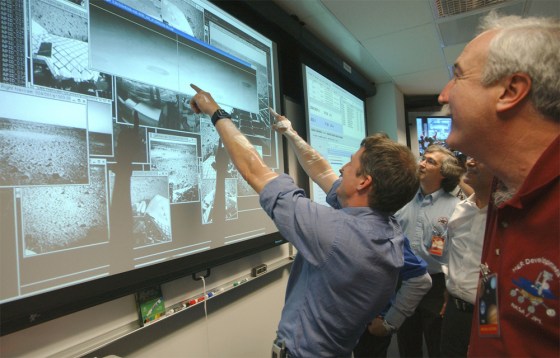 NASA Administrator Sean O’Keefe, right, and Principal Investigator Steve Squyres, pointing at screen, examine the first images arriving from Mars after the landing of the Spirit rover on Saturday night.