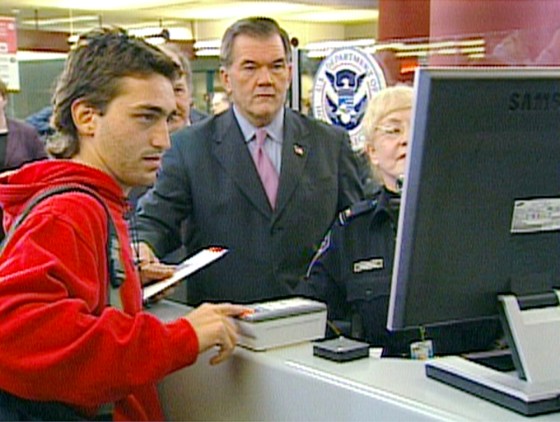 Secretary of Homeland Security Tom Ridge watches as a foreign visitor gets fingerprinted and photographed at a US-VISIT station at Atlanta's airport.