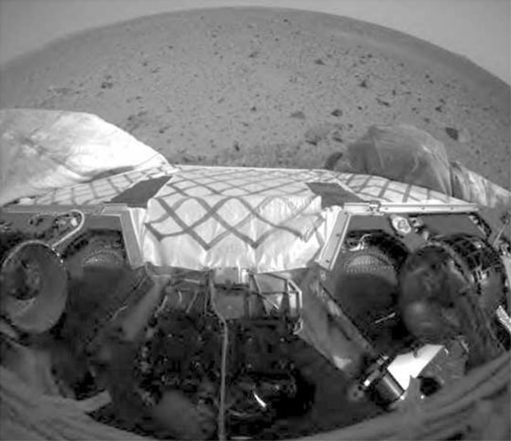 This wide-angle image from the Spirit rover's front hazard avoidance camera shows the rover's wheels after a "stand-up" procedure, completed in preparation for rolling off the landing platform next week. The two wheels on the bottom right and left are locked into position, along with the suspension system. The Martian landscape lies beyond.
