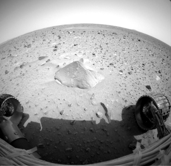 A wide-angle view from one of the Spirit rover's navigation cameras shows a Martian rock named "Adirondack" at center stage, with the rover's wheels in the foreground. Adirondack is about 14 inches wide and 8 inches high.