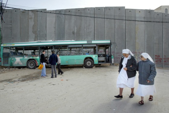 Nuns walk past an Israeli bus, destroyed in Sunday's suicide bombing and placed next to a section of the separation barrier, in the West Bank village of Abu Dis on Tuesday.