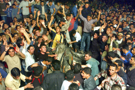 Angry Palestinians gather around a car in Gaza on Saturday after it was struck by an Israeli missile.