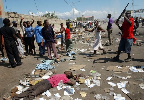 A man gestures with a shotgun as looters make their way to the port past a dead man in Port-au-Prince on Feb. 27.