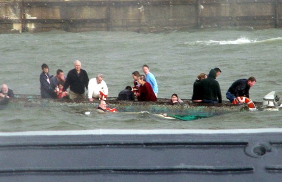 Passengers cling to the hull of a capsized pontoon boat in Baltimore's Inner Harbor as a U.S. Navy boat approaches to assist in rescue operations, on Sunday.