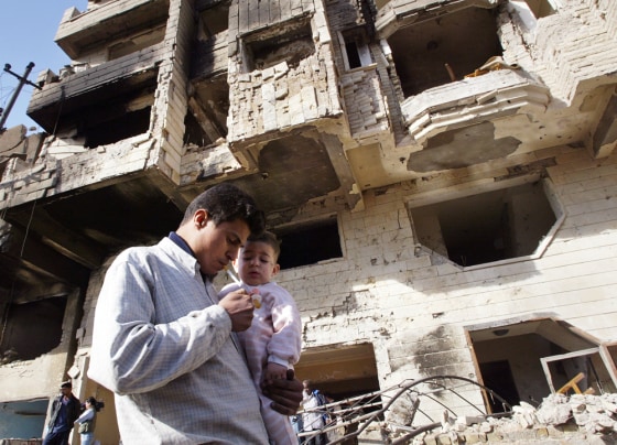 An Iraqi man holding his child walks Thursday past the site of an explosion that tore apart a five-story in Baghdad.