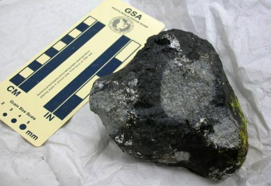 This Chicago-area meteorite fragment, collected in 2003, is shown with a scale of inches and centimeters for reference. It was embedded in the street. Note the yellow paint on the far right side, picked up on impact.