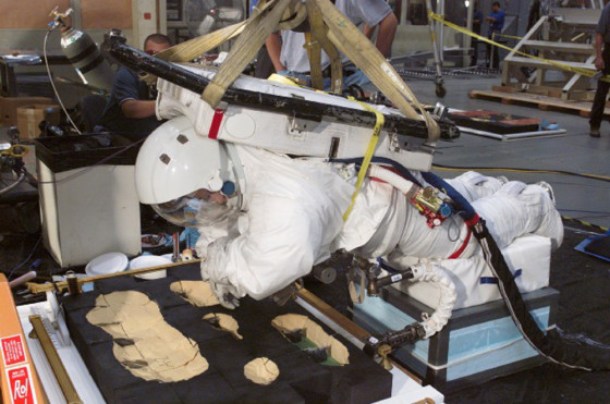 EVA Operations Engineer Dana Weigel, dressed in a spacesuit, participates in an evaluation of shuttle tile repair techniques in the Space Environment Simulation Laboratory at NASA's Johnson Space Center. The board is a simulated section of tile, with dense yellow foam as a substitute for the tiles.