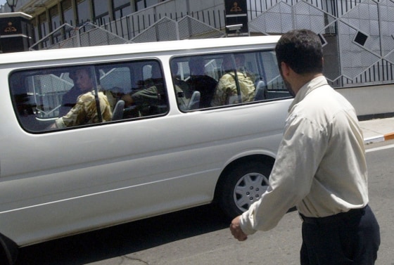 Eight British servicemen sitting inside a vehicle are watched by an Iranian security&nbsp;guard as they arrive at Mehrabad airport in Tehran, Iran on Thursday.