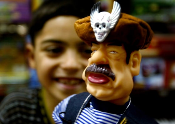 IRAQI BOY LOOKS AT SADDAM HUSSEIN DOLL IN A BAGHDAD SHOP