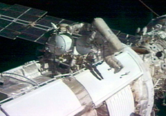 Spacewalkers Mike Fincke and Gennady Padalka huddle over a pump control panel on the exterior of the international space station Friday, with a solar panel stretching away in the background.