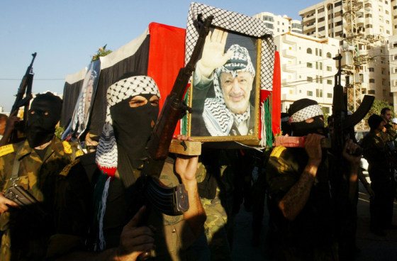Masked Palestinian militants carry a coffin covered with the Palestinian flag and posters of president Yasser Arafat during a mock funeral in Gaza