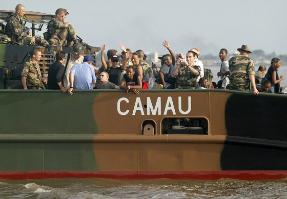 Foreigners traveling by boat wave Saturday as they leave for the airport at Abidjan, Ivory Coast. The foreigners, many of them longtime Ivory Coast residents, piled into buses, boats and planes Saturday as a French-run evacuation built despite government promises to quell a surge of anti-French violence.