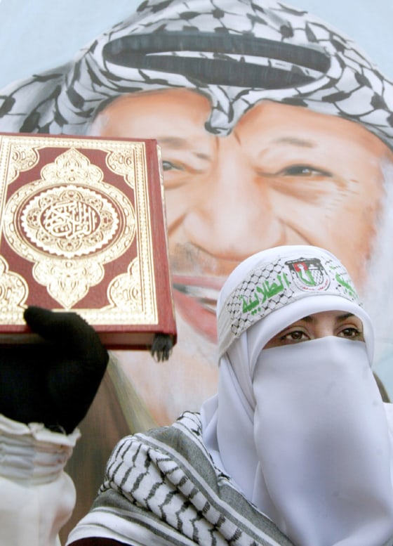 Palestinian woman supporter of Fatah movement holds a copy of the Koran in front of a poster of late Palestinian leader Arafat in nablus