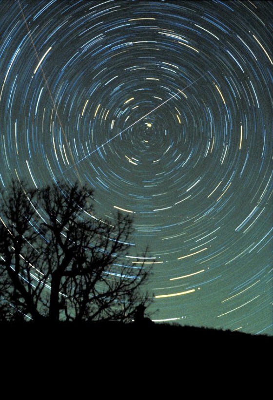 A Geminid meteor streaks across the night sky, with circular star trails whirling the background, in a time-exposure photo made by astronomer Jimmy Westlake in December 1985.
