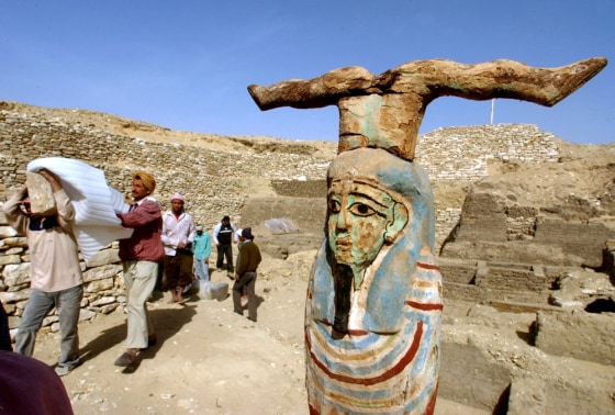A statue showing Petah Sakar, the god of the cemetery, stands at right as Egyptian workers carry an ancient wooden coffin shaped like a human body through an archaeological site Wedhesday. The coffin dates back to the 26th Dynasty, between 672 B.C. and 525 B.C.