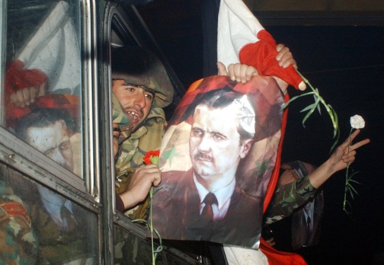 Syrian troops withdrawing from Lebanon display Syrian flags along with posters of President Bashar Assad as they cross the Syrian-Lebanese border early Saturday.