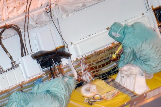 Inside Discovery's hangar at the Orbiter Processing Facility, workers remove wire tray covers on Discovery and add extra padding on Friday.