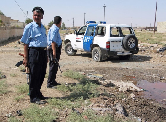 Police officers stand next to a damaged police vehicle after roadside bomb attack in Kirkuk