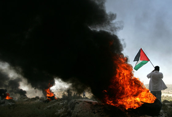 Burning tires release black smoke as a man waves a Palestinian flag Wednesday during a protest against the construction of a section of Israel's barrier in the West Bank village of Bil'in. 