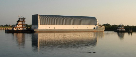 A tugboat pushes the Pegasus barge away from the dock at the Launch Complex 39 area in Cape Canaveral, Fla., just after dawn Tuesday. The barge is carrying the external fuel tank for the next shuttle mission. In the foreground, an alligator just barely peeps above the water's surface.