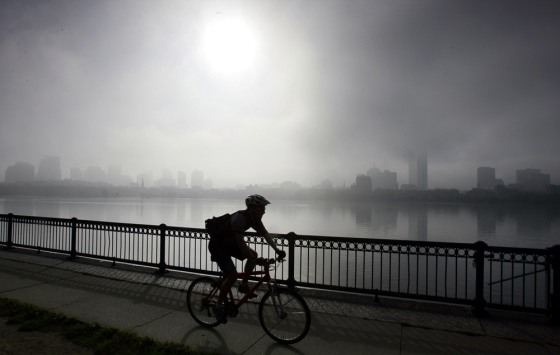 Cyclist rides along Charles River as the fog lifts from the Boston skyline in Cambridge