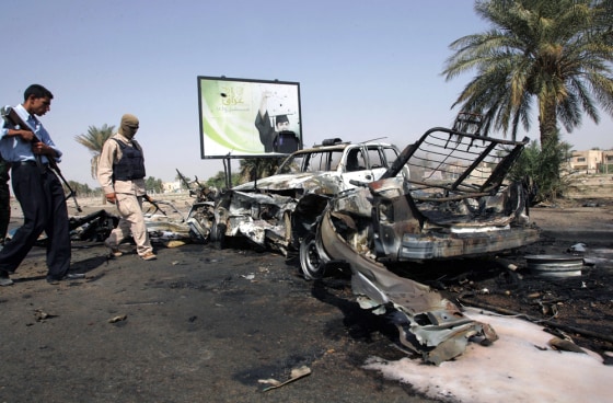 Iraqi policeman and soldier look at destroyed vehicles following attack on checkpoint in Baghdad