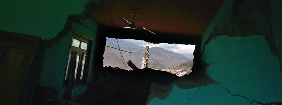 A man looks through a hole in an earthquake-destroyed home in Sanger, Pakistan, on Wednesday. Across the region of northwest Pakistan destroyed by an earthquake, hundreds of villages remain cut off from help.