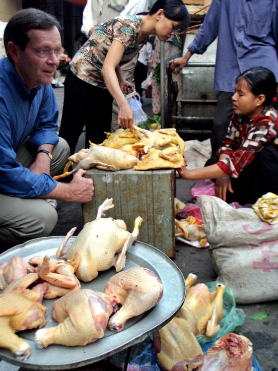 US Health Secretary Leavitt sits next to slaughtered chickens on sale at Hang Be market in downtown Hanoi