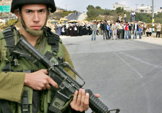 An Israeli soldier stands guard in front of Palestinians as they wait to be permitted to cross at El-Khader junction near Bethlehem
