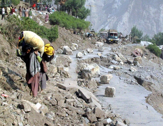 Kashmiri earthquake survivors carry relief goods as they walk through a damaged road in Neelam Valley