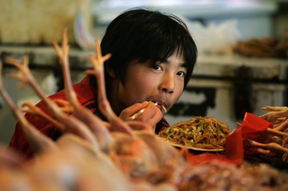 A young Chinese man eats next to freshly killed chickens at his chicken stall in a Beijing market on Oct. 28.