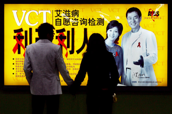 A Chinese couple wait at a subway station in front of an AIDS awareness campaign poster in Beijing
