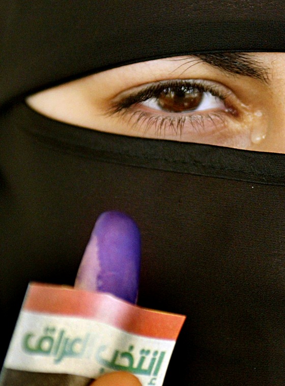A veiled Iraqi woman reacts as she shows off her finger stained with blue ink at a polling station in Amman