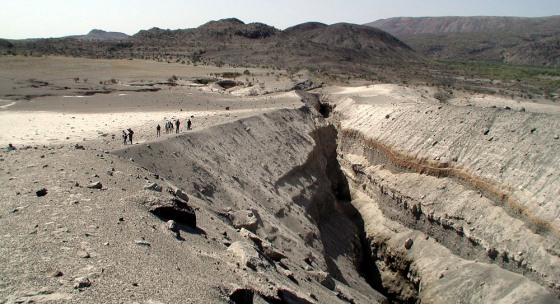 Researchers stand on the brink of a steep slope leading down to a fissure in the Ethiopian desert, in a barren region called Boina or Dabbahu.