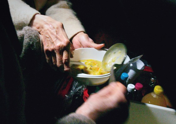 Volunteers pour pork soup into a plastic bowl during a free soup distribution to the homeless in Paris.