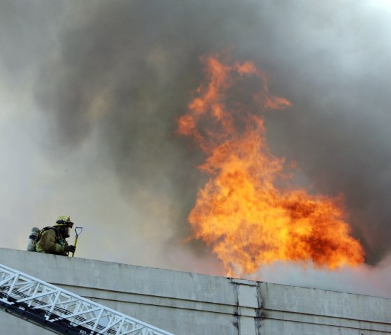 A firefighter takes a rooftop position at a two-story commercial building fire in downtown Los Angeles on Monday. The fire was fanned by high winds and required more than 100 firefighters to put it out.