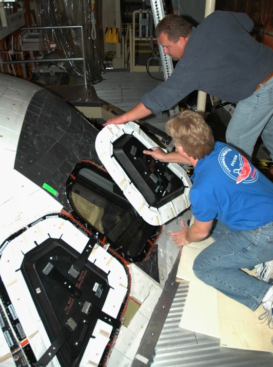 Shuttle technicians remove the hard cover from a window on the Discovery orbiter to let crew members to inspect the window from the cockpit.