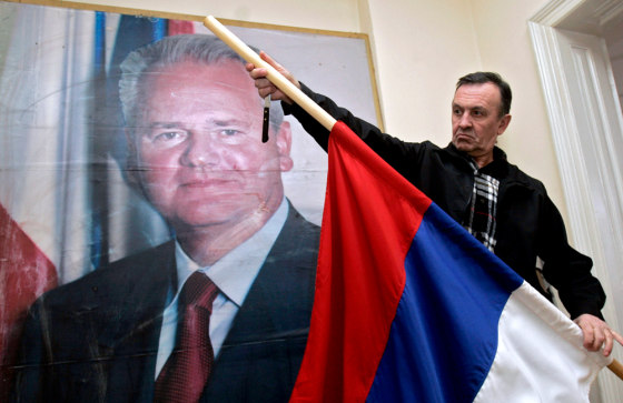 An activist of a Slobodan Milosevic support group, "Freedom," flag to half staff in front of a poster of the former <a href=http://msnbc.msn.com/id/12083338/>Yugoslav leader at the group's</a> headquarters in Belgrade, on Saturday.