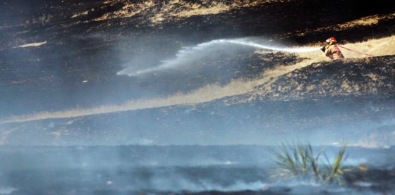 A firefighter sprays water on burning and smoldering grass North of Pampa, Texas, on Monday.